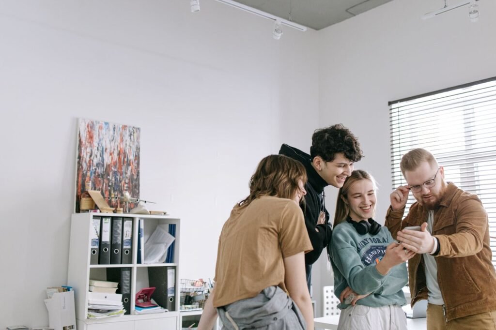 A group of young adults smiling and enjoying a moment together in a bright, modern office environment.